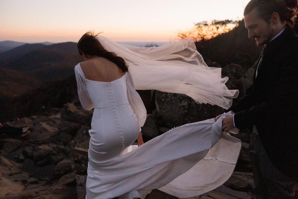 A groom holds his brides dress as the wind gusts and tries to whip it around