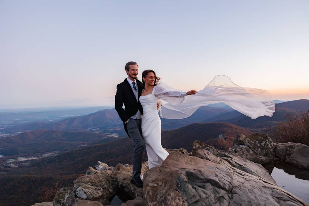 A bride holds her veil as the wind blows it. at the top of Stony Man Summit at sunrise