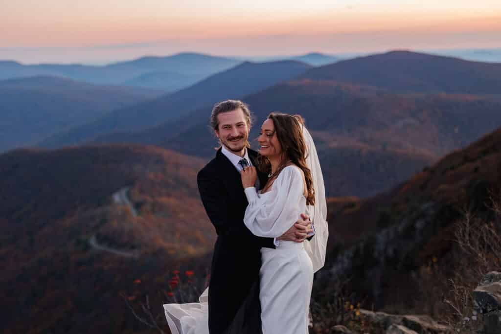 A bride and groom laugh about the gusts of wind blowing them and their wedding attire around during their sunrise elopement