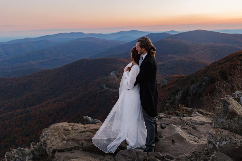 A bride leans into her groom as they admire the view of the sun rising during their elopement at Stony Man.