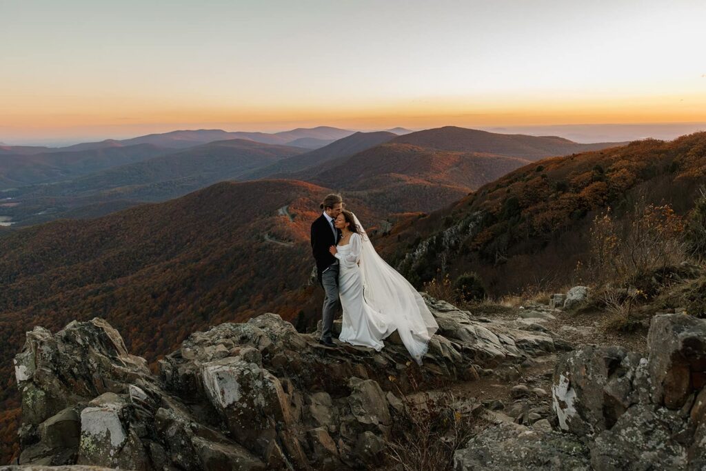 A groom  kisses his brides forehead while she leans into him during their sunrise elopement in front of the 
Blue Ridge Mountains
