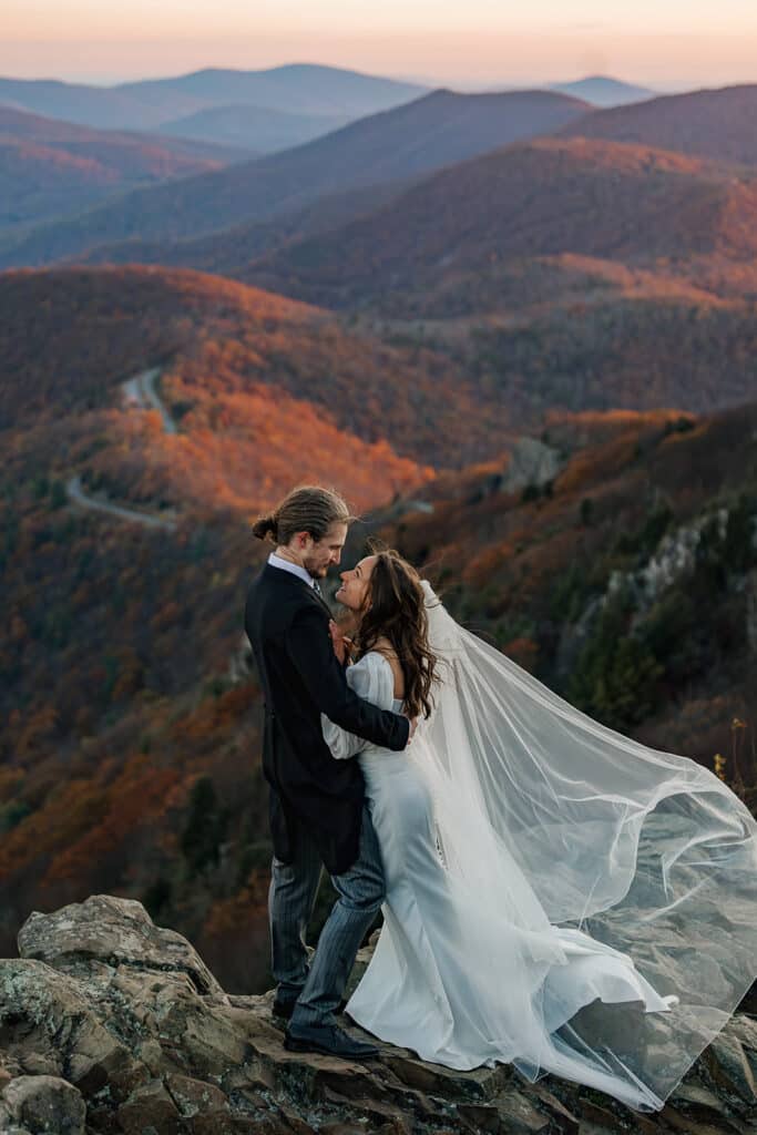 A bride and groom smile at one another, and try to keep each other warm during their sunrise elopement
