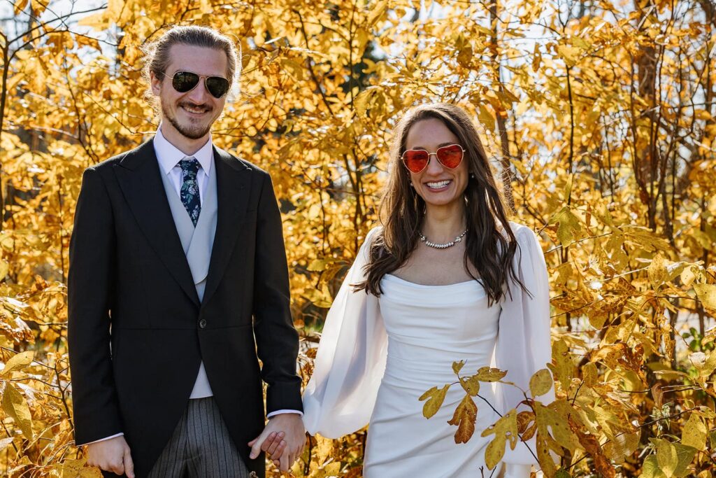 A bride and groom wearing sunglasses stand in front of bright yellow leaves at Shenandoh