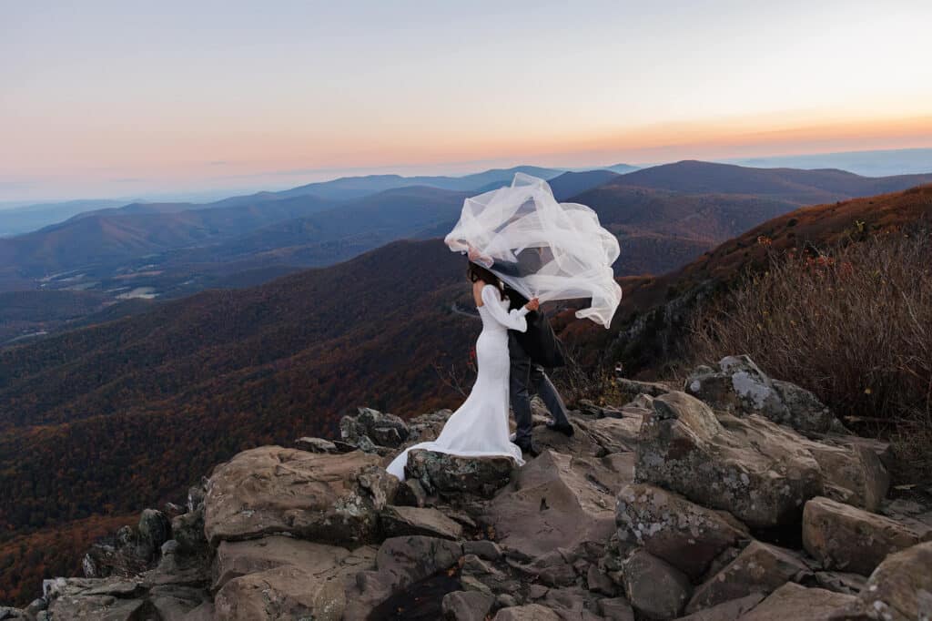 A groom tries to hold onto his brides veil as the wind whips it around and over both of their heads