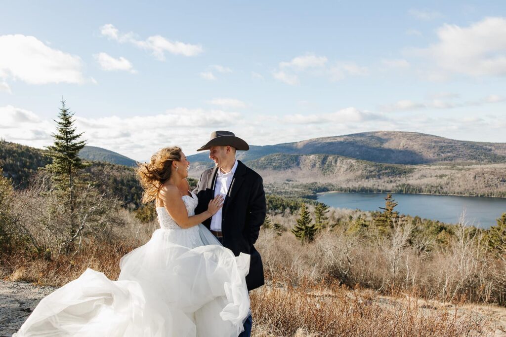 A bride and groom laugh as the wind whips the brides dress during their wedding day.