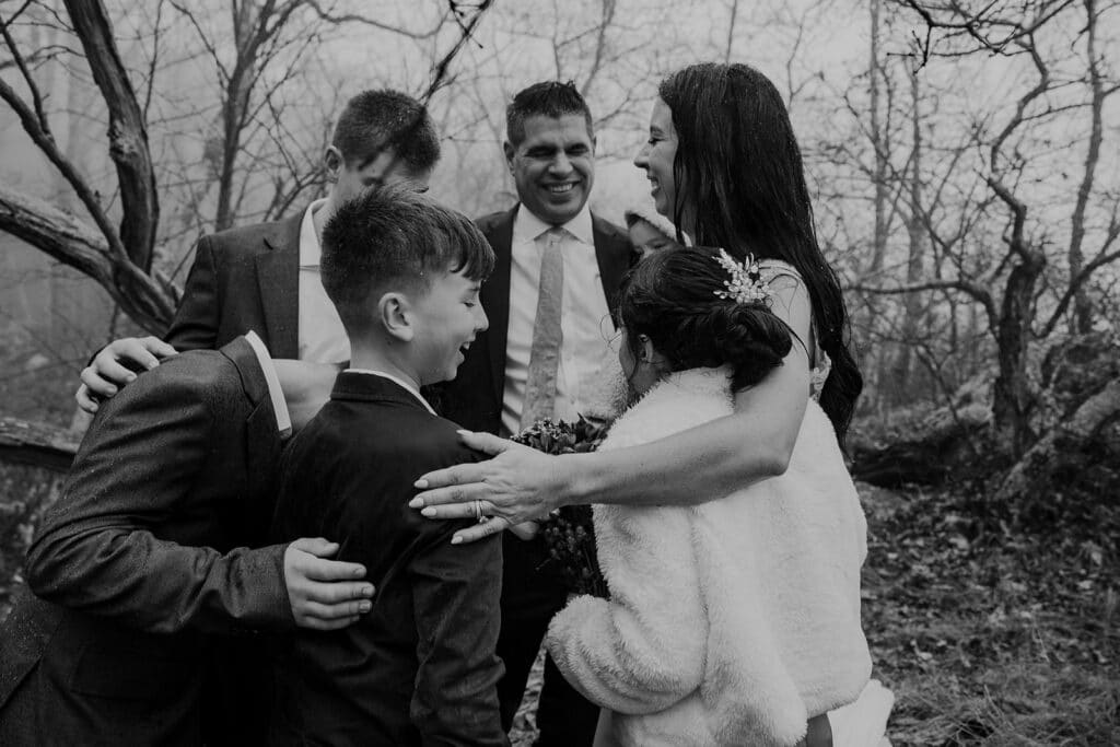 A newly blended family laugh through the raindrops during their elopement ceremony. The family chose to laugh and embrace the pouring rain