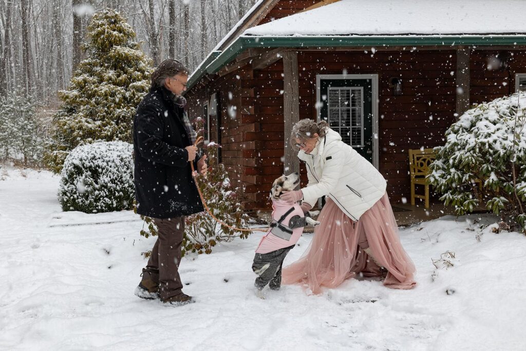 A dog greets the bride with excitement on the couples elopement day during their first look in front of. cabin in the snow