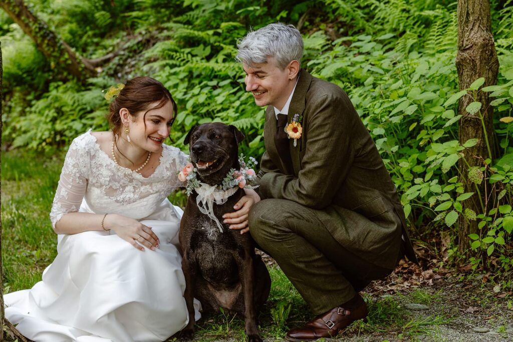 A bride, groom, and their dog smile with joy on their wedding day