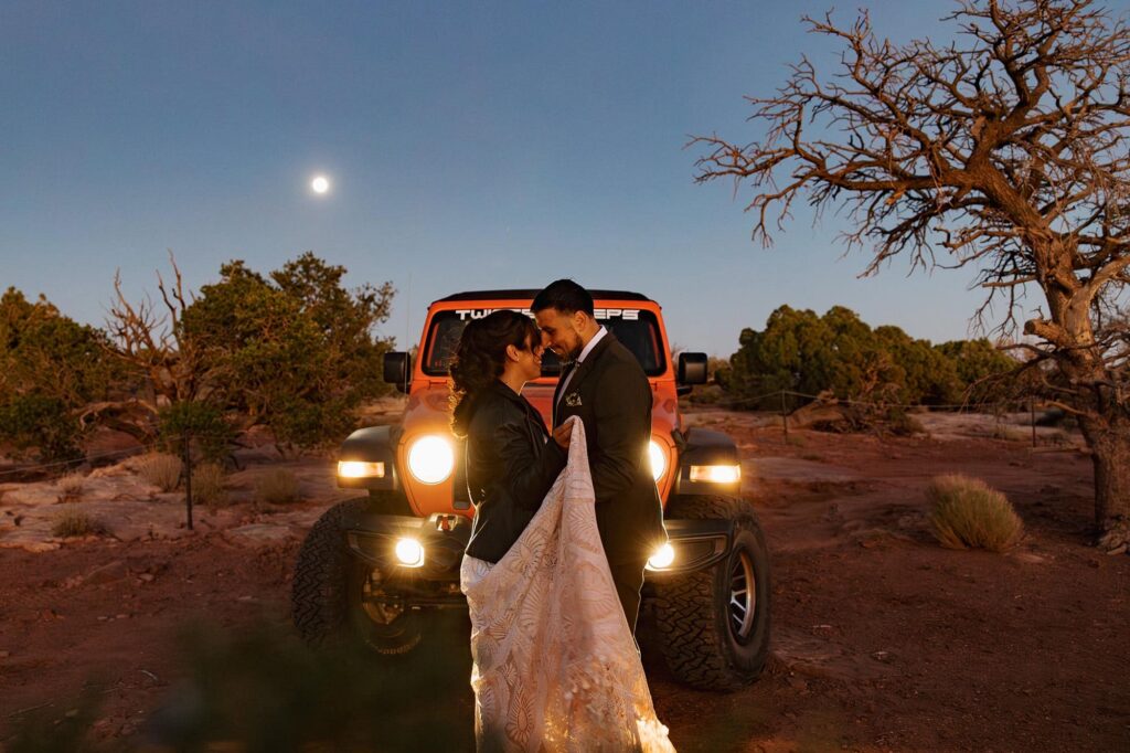 A bride and groom share their first dance in front of their jeep lights during their desert elopement