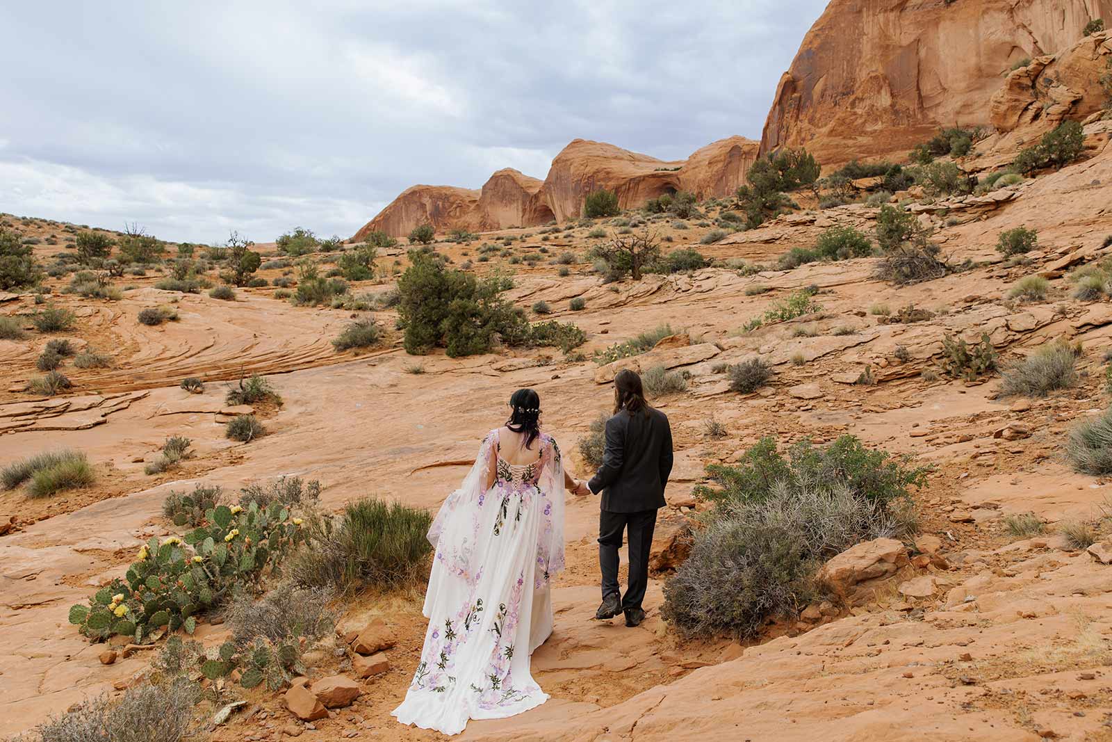 A bride and groom walk through the desert holding hands during their sunset elopement in Moab