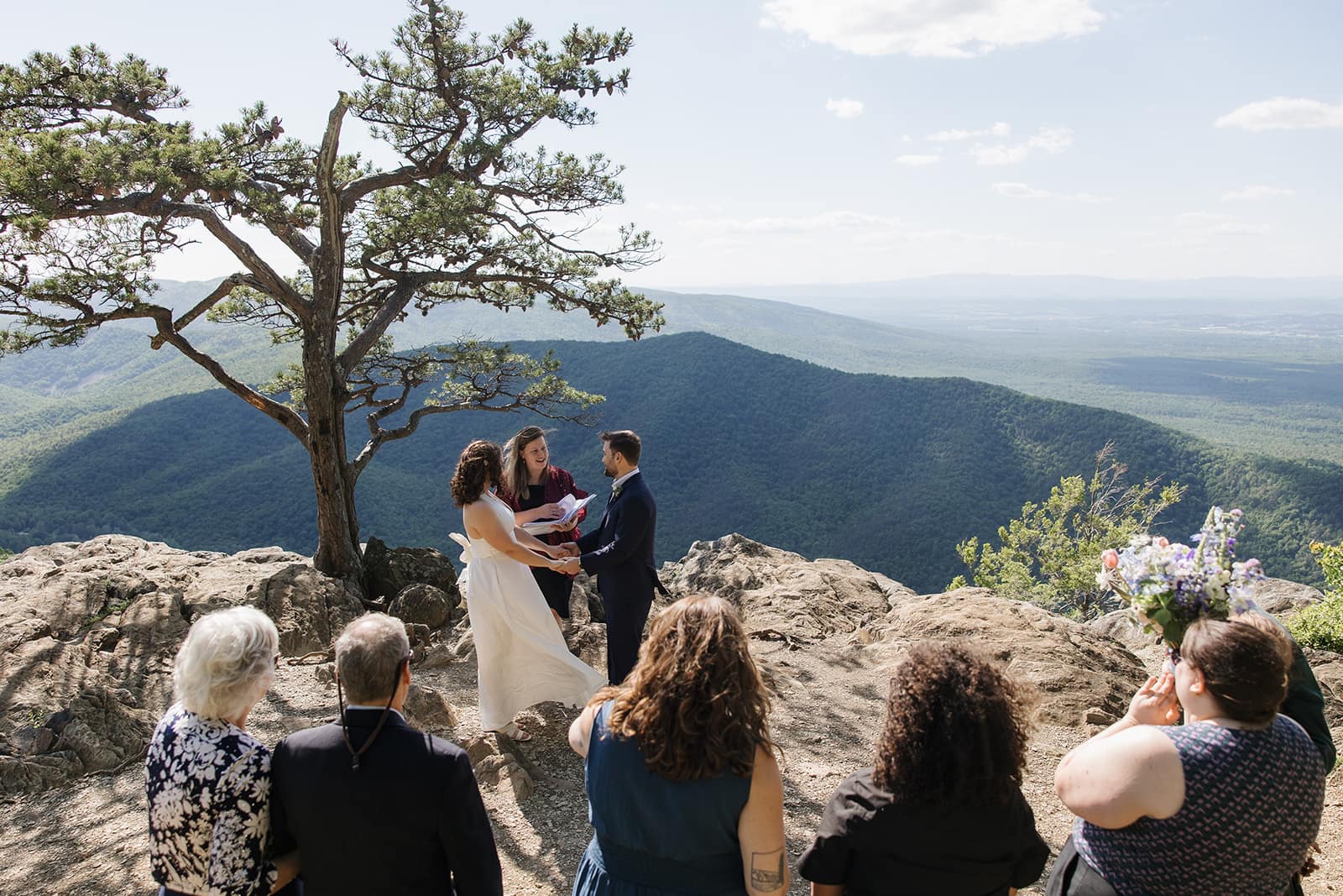 A bride and groom stand at an overlook during their elopement with family