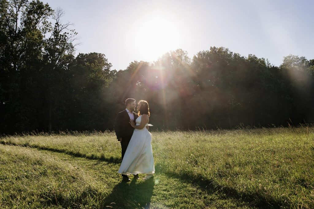 A bride and groom stand facing each other as the sun flares behind them during their wedding at Indigo House in Virginia
