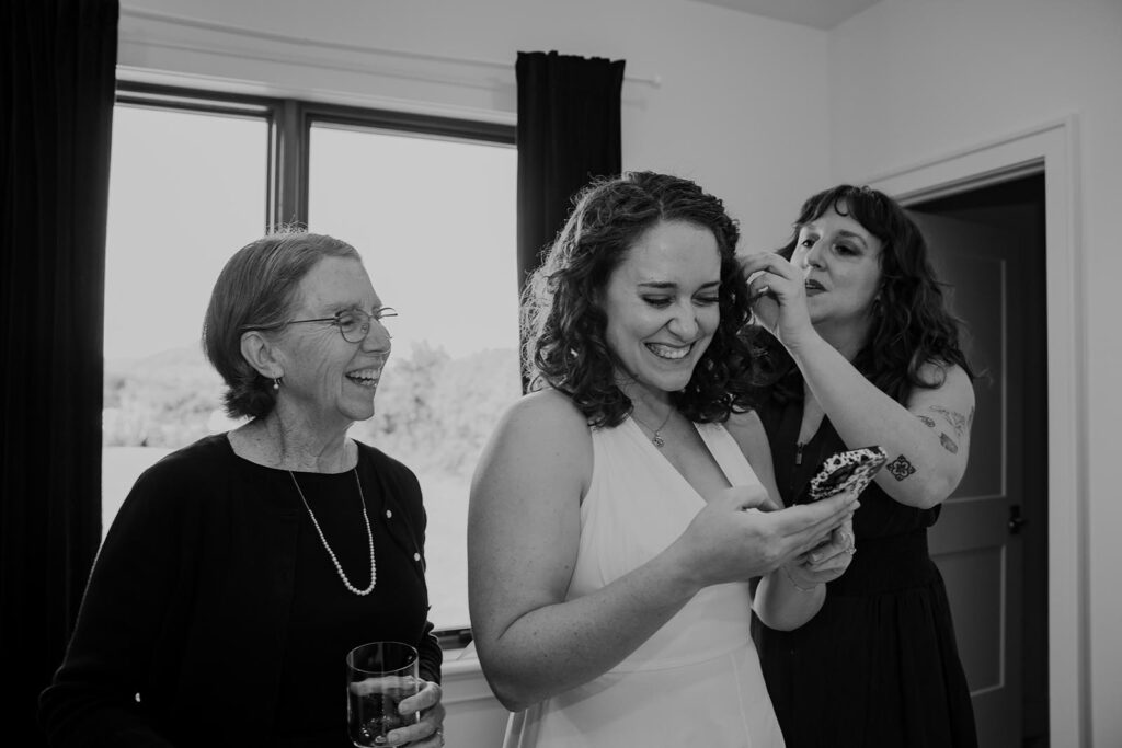 A bride smiles as her mom and sister finish putting on her dress on her elopement day