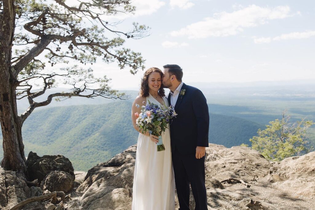 A groom kisses his bride on the cheek before their elopement ceremony at Raven's Roost in Virginia