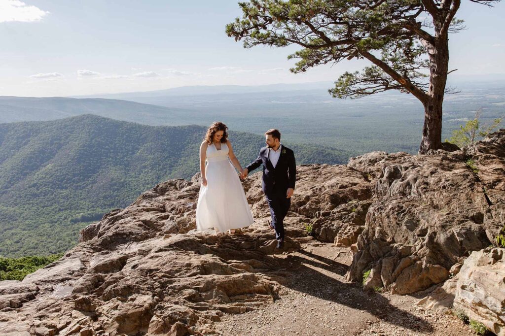 A groom leads his bride over a rocky section of Raven's roost during their adventure elopement in Virginia