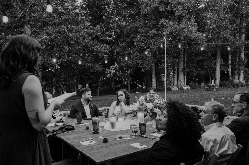 A bride and her closest family listen to a speech being given by her sister during their outdoor intimate wedding reception at indigo house