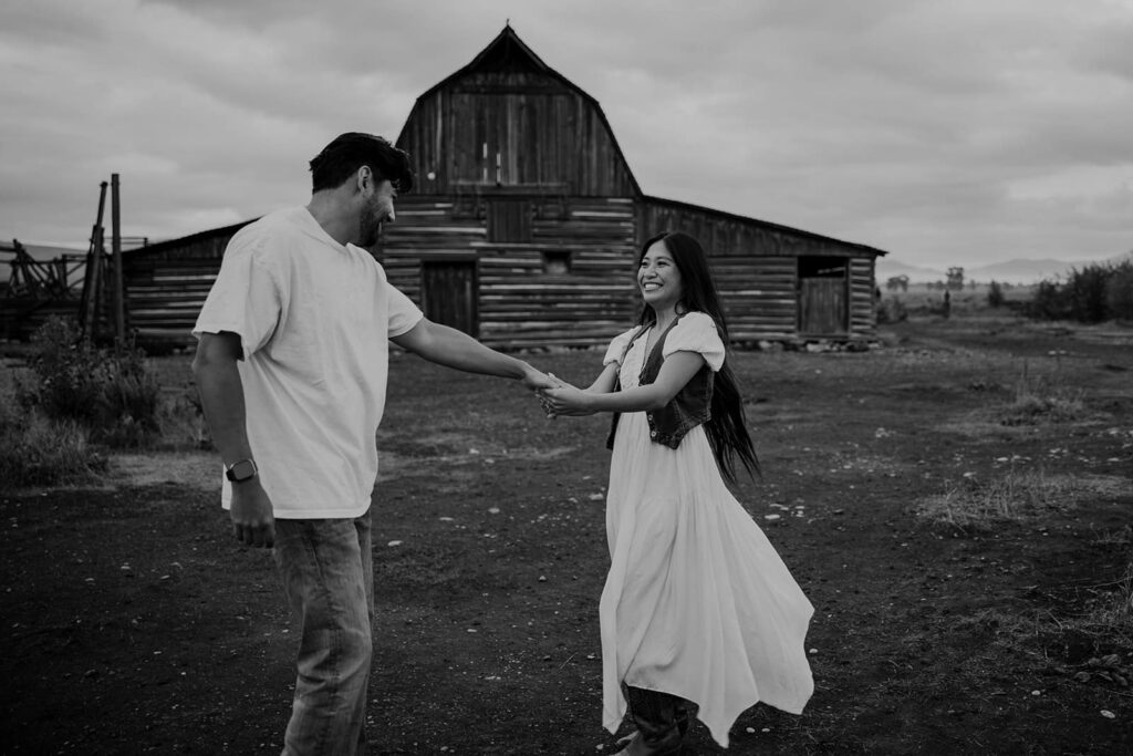 A photo of a couple in front of the barn at Mormon Row at sunrise at their Grand Teton National Park engagement session