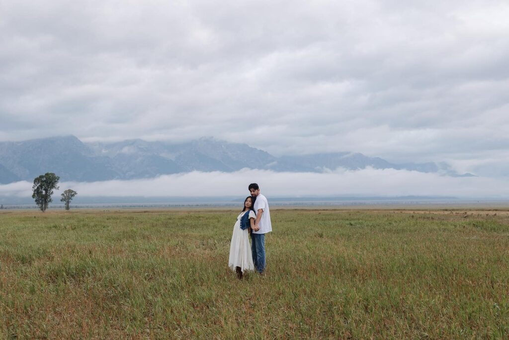 A couple stands in front of the Grand Tetons during their sunrise engagement session at the Gradn Tetons