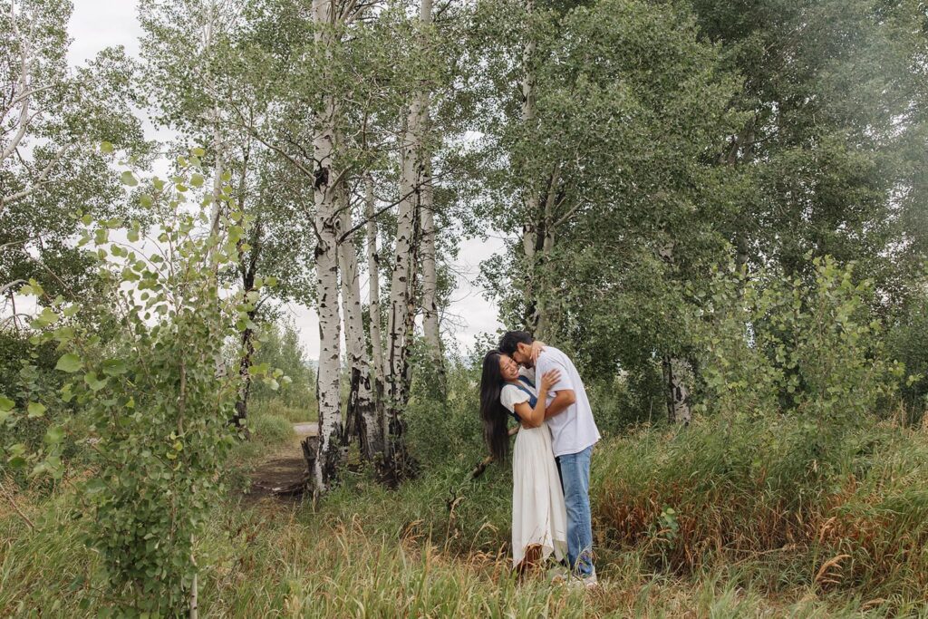 A couple stands in front of some aspen trees at Mormon Row in Grand Teton National Park during their sunrise engagement session