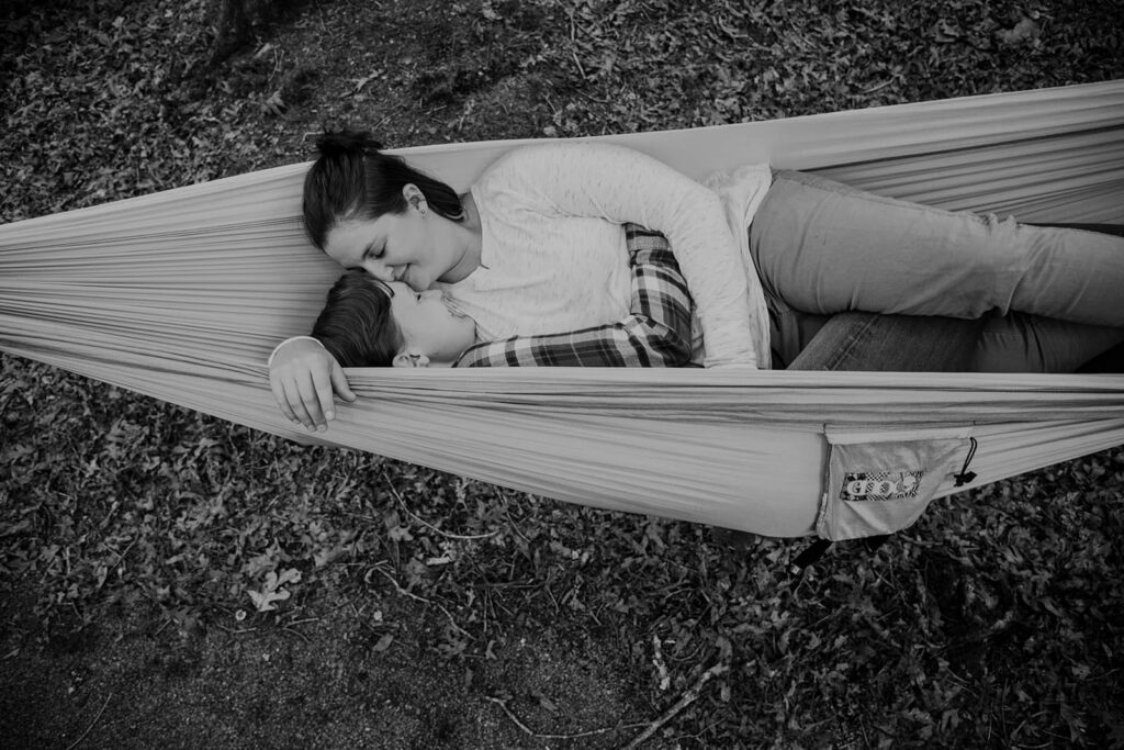 A couple snuggles in a hammock while camping. The photo is black and white, and is taken from above