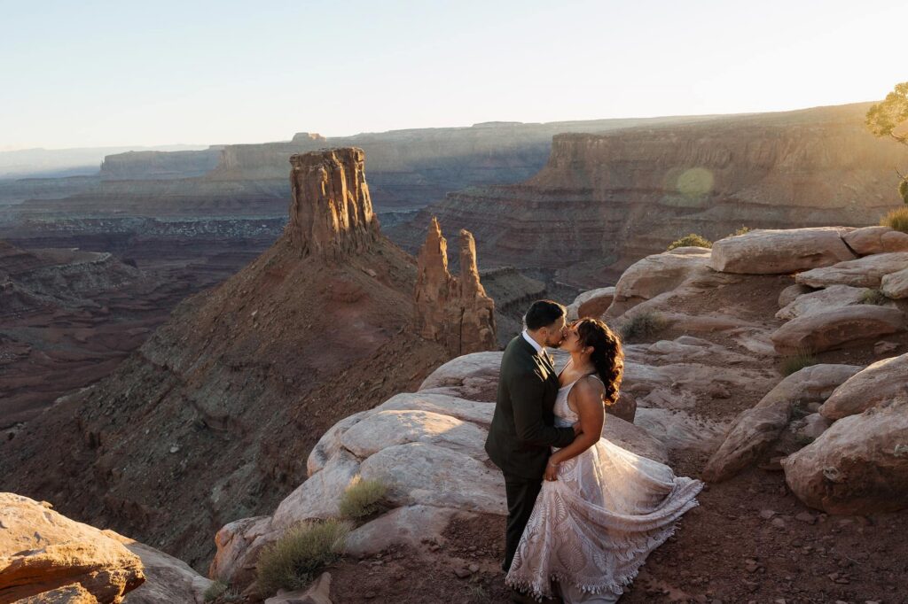 A bride and groom kiss while the sun sets in the red rocks during their elopement ceremony