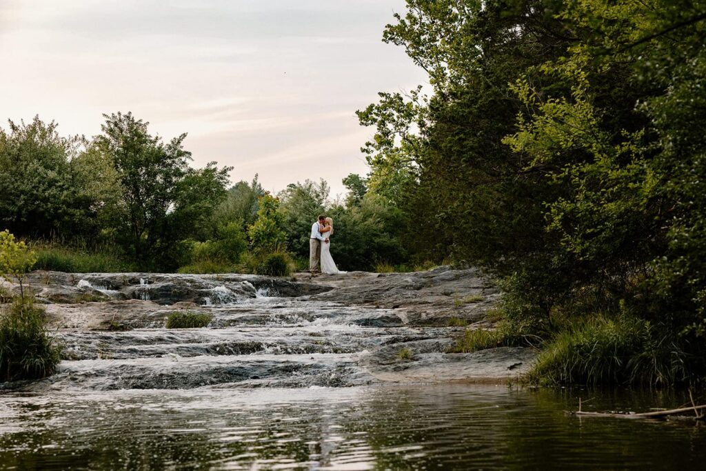 A bride and groom stand at the top of a waterfall during their full-day elopement