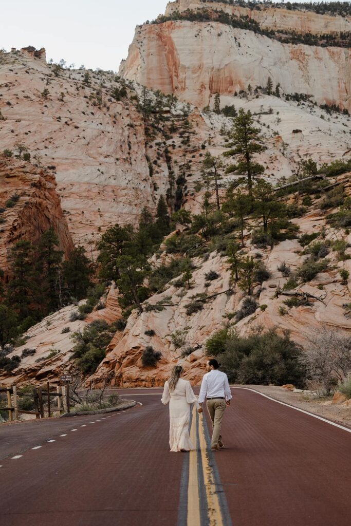 A bride and groom walk on the yellow lines of the road at Zion National Park during their elopement. Zion National Park is one of the best places to elope in Utah