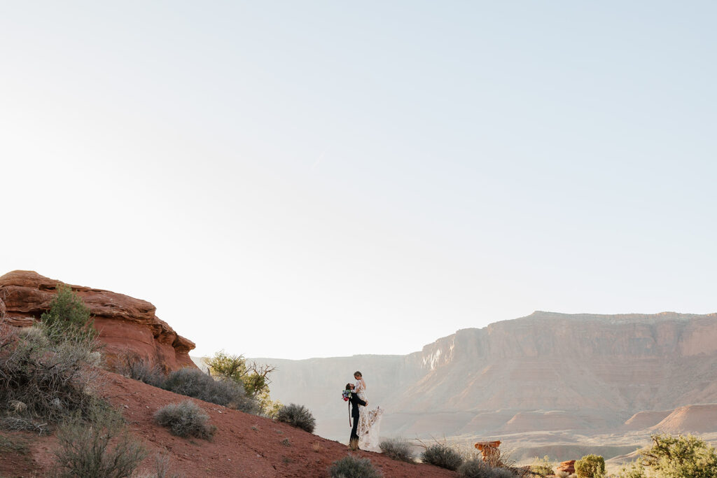 A groom lifts his bride in the middle of the desert in Moab to celebrate their elopement. Moab is one of the best places to elope in Utah.